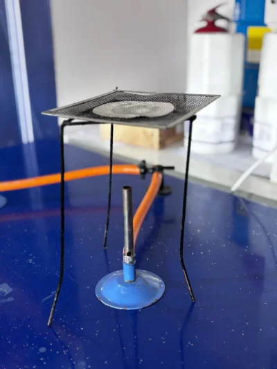 Bunsen burner connected to an orange gas hose, under a tripod stand with wire gauze