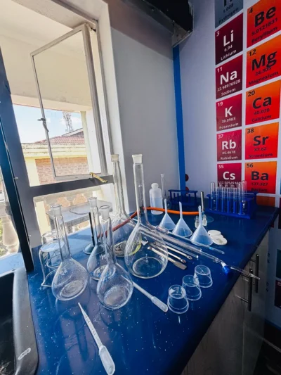 Volumetric flasks, filter funnels, watch glasses, test tube racks and droppers on a bench by a periodic table