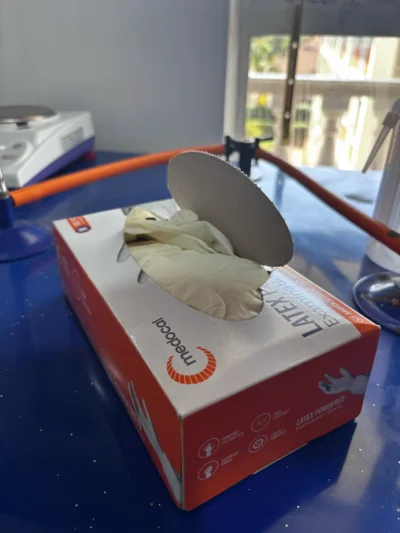 Open box of latex examination gloves on a blue bench next to a gas tap