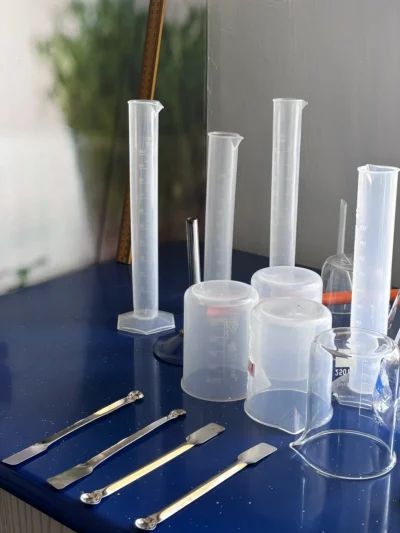 Plastic measuring cylinders, plastic and glass beakers and four metal spatulas on a blue bench