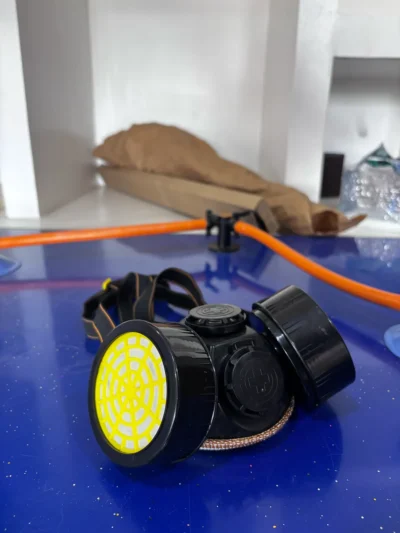 Black twin-filter respirator mask with a yellow filter cover on a blue bench