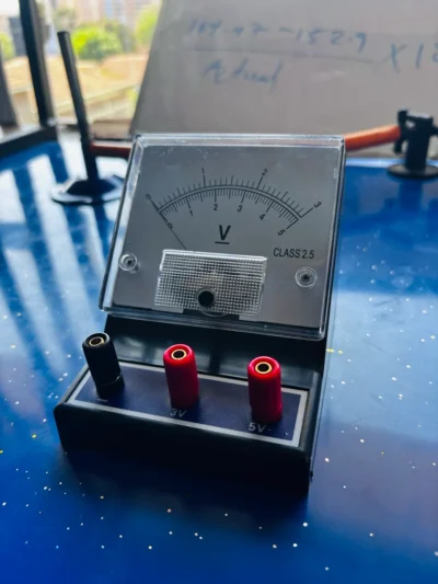 Analogue voltmeter with 3 V and 5 V terminals on a blue bench